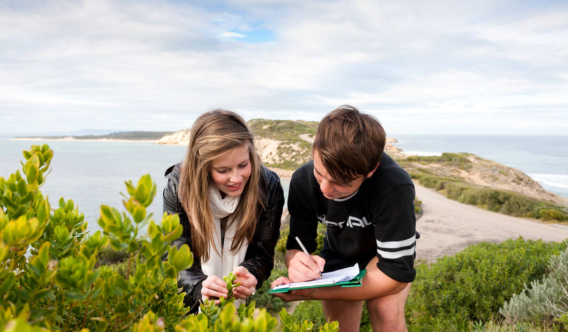 Two teenage children studying plants and making notes