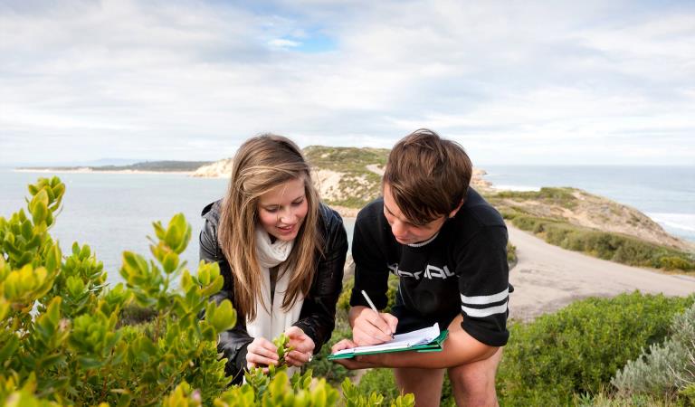 Two teenage children studying plants and making notes