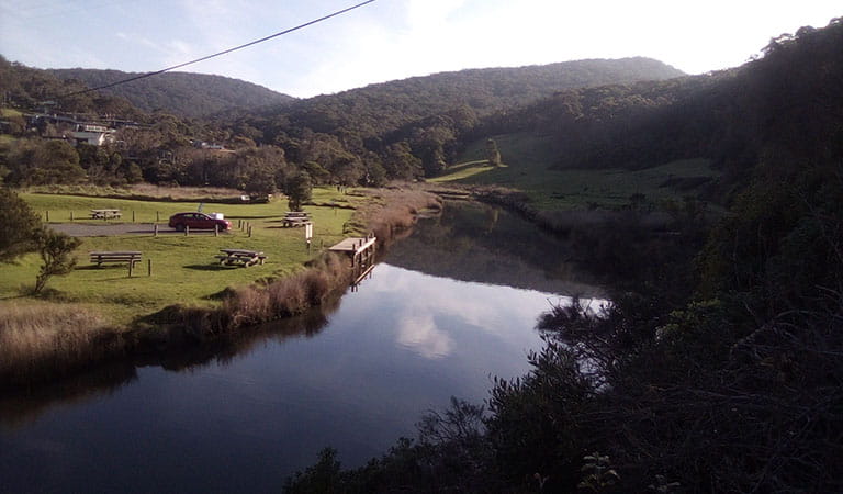 A river flowing between bush and farm land.