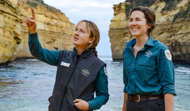 Two rangers observe something out of shot in a coastal scene. 