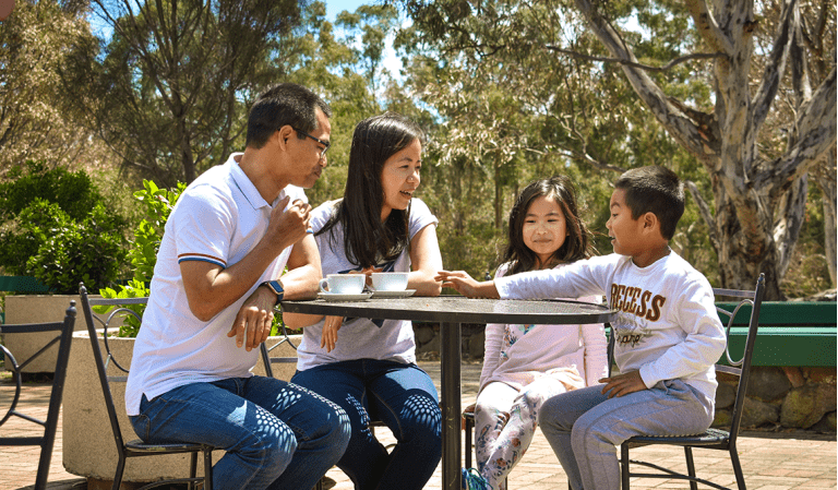 A mother, father and two primary-aged children sit outside with coffees at Brimbank Park