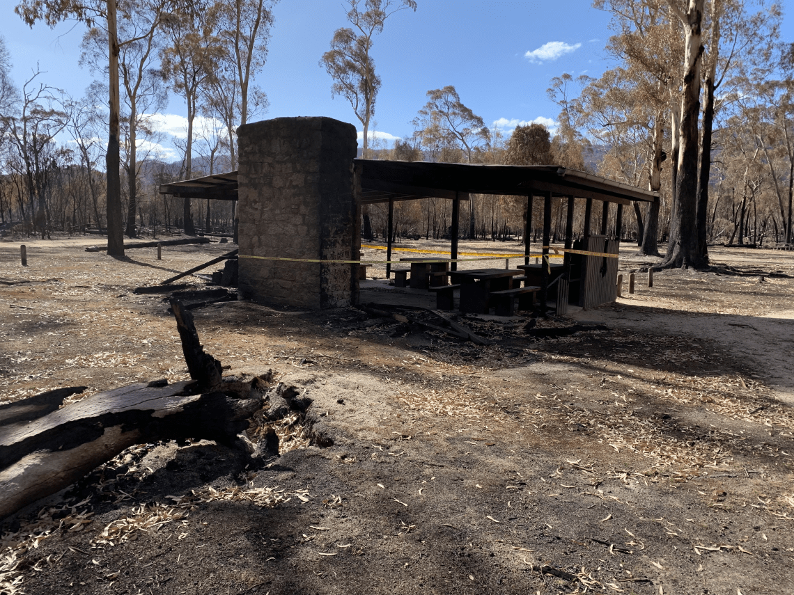 A small shelter with picnic tables blackened by fire damage