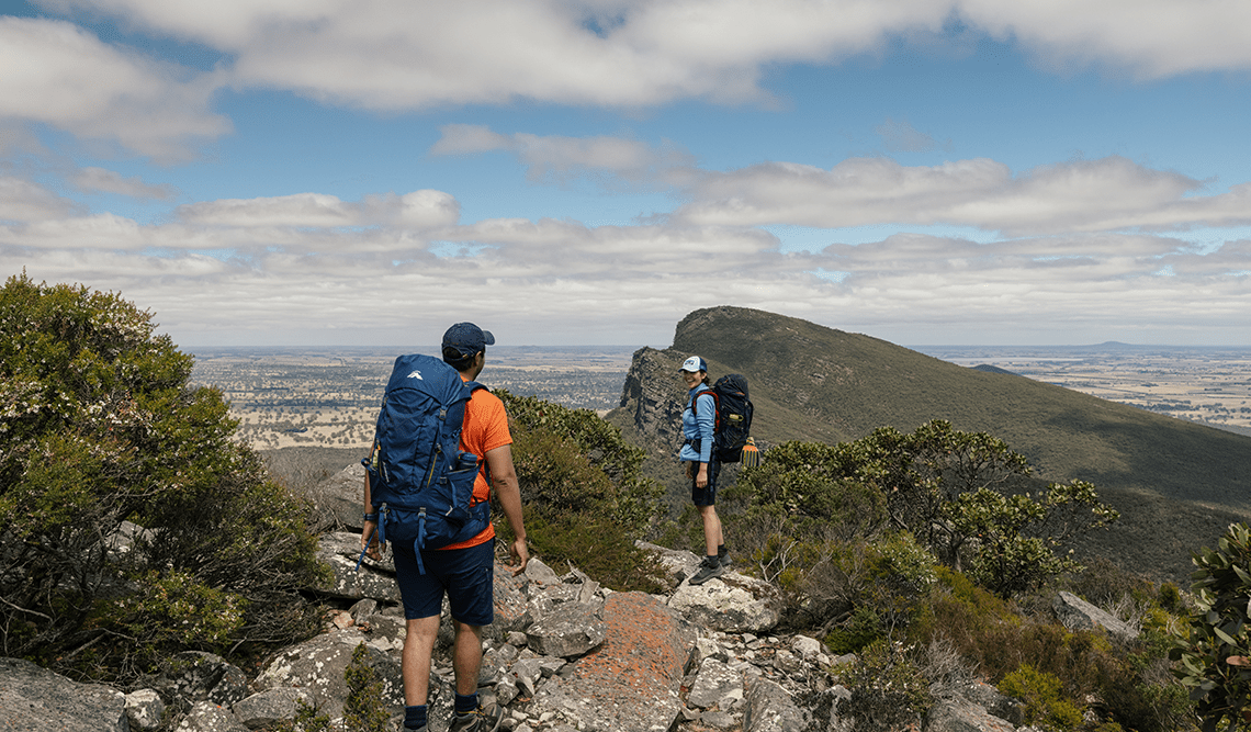 A man and a woman with hiking packs enjoy summit views Signal Peak, Grampians Peaks Trail, Grampians National Park