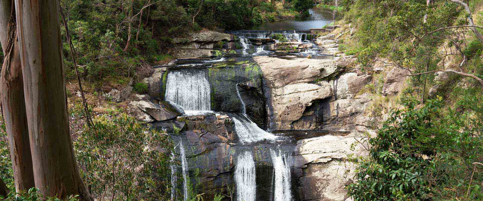 A three tiered waterfall in full flow set amongst a rugged bushlands