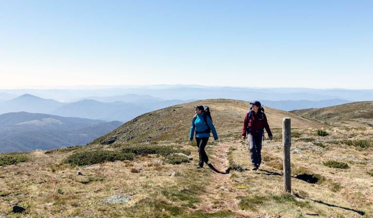 Two women walk towards the summit of Mt Bogong in the Alpine National Park.