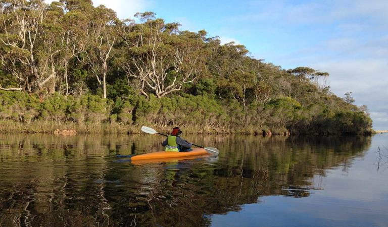 A women in a bucket hat kayaks along Wingan Inlet.