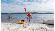 A woman holding a paddle walks up the beach with her kayak on the beach behind her 