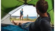 A man looks out of his tent towards his partner walking towards him with the coast in the background at Johanna Beach in the Great Otway National Park.