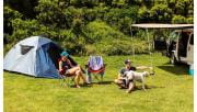 A couple in their thirties play with their dog at Johanna Beach Campground next to their tent and campervan.