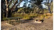 A campfire and picnic table near the river's edge at Ackle Bend Campground in Little Desert National Park