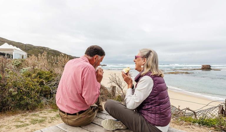 An older couple stop to enjoy a pastry above Sorrento Back Beach on the Mornington Peninsula.