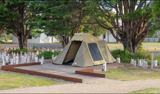 A tent set up on wood flooring in a coastal landscape. A ramp leads to the entrance.