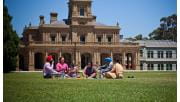 A family share a picnic on the foreground of Werribee Mansion.