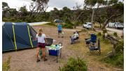 A man walks towards a women who is cooking at a stove next to their tent at Tidal River Campground at Wilsons Promontory National Park