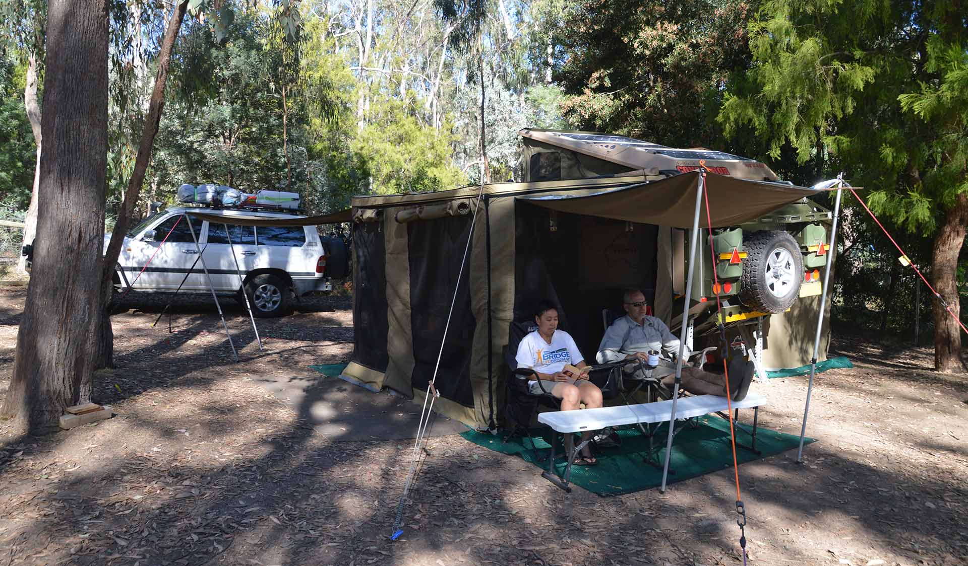Two friends relax under the shelter of their camper trailer at Fraser Camping Area in the Lake Eildon National Park.