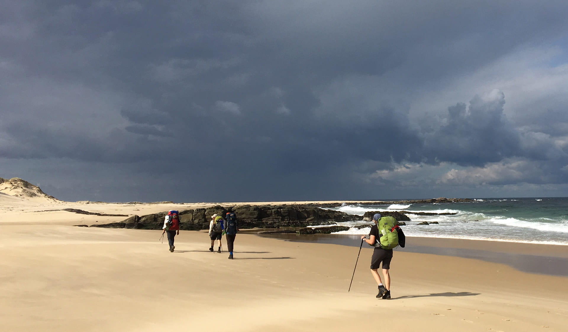 Three friends hike along the coastline at the Cape Howe Wilderness Zone as part of the Wilderness Coast Walk.