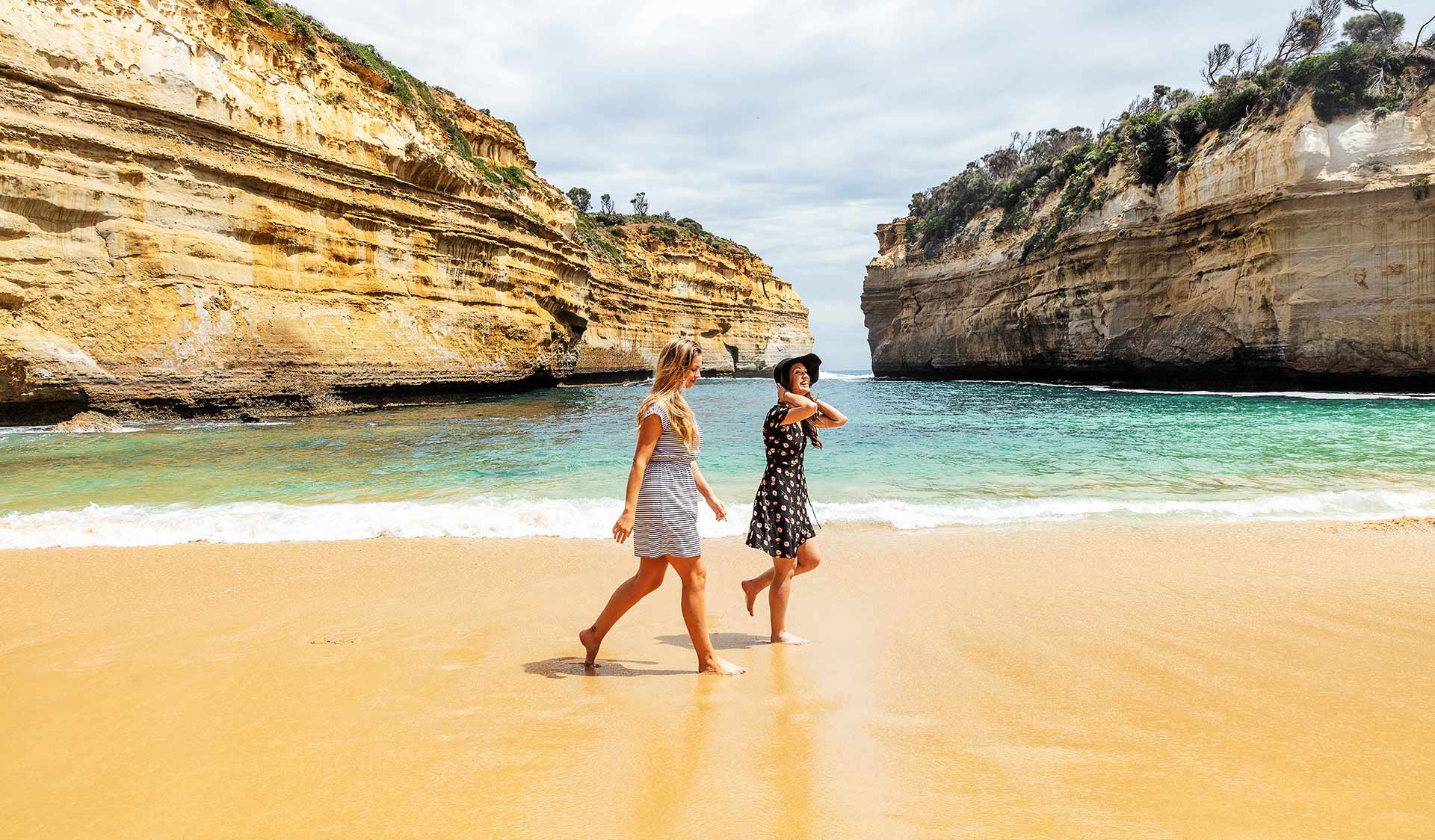 Two young wearing dresses stroll across the beach at Loch Ard Gorge.