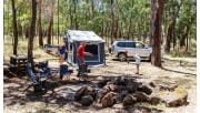 A family of four gathered and playing football at a camp set up between trees with equipment, facilities, and car in the background.