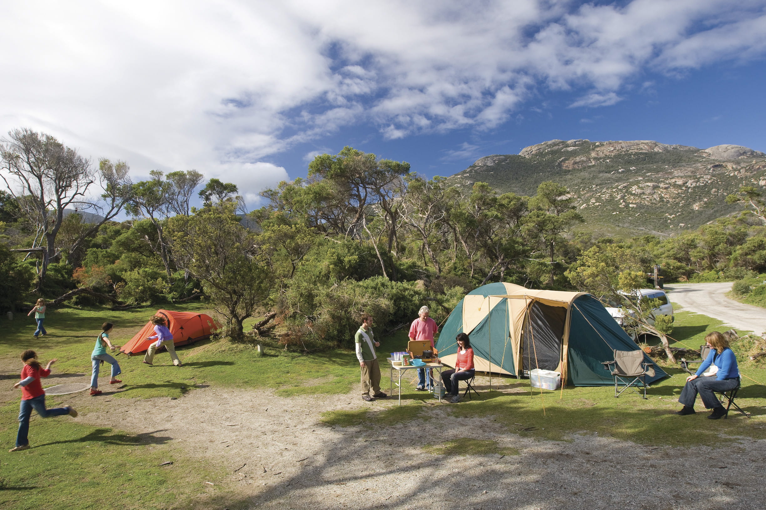 Adults sitting and children playing in front of two tents, with mountain in background at Wilsons Promontory National Park