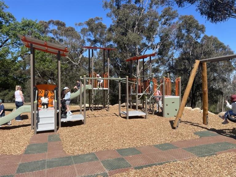 Children and adults playing on the new playground.  Blue sky and eucapypts in the background.