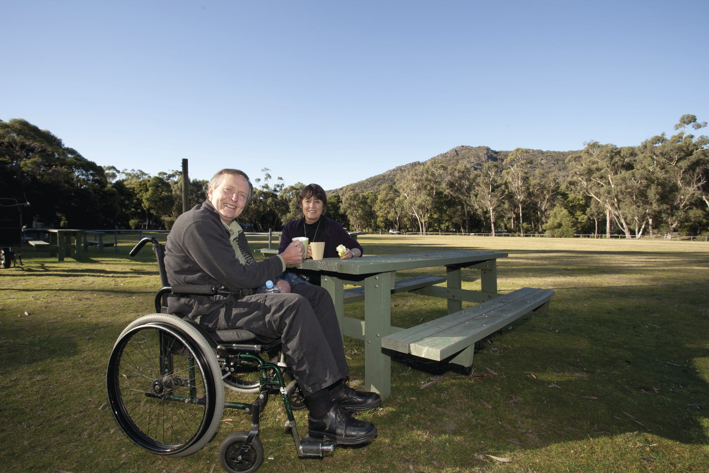 Man in wheelchair and woman sitting at picnic table in park