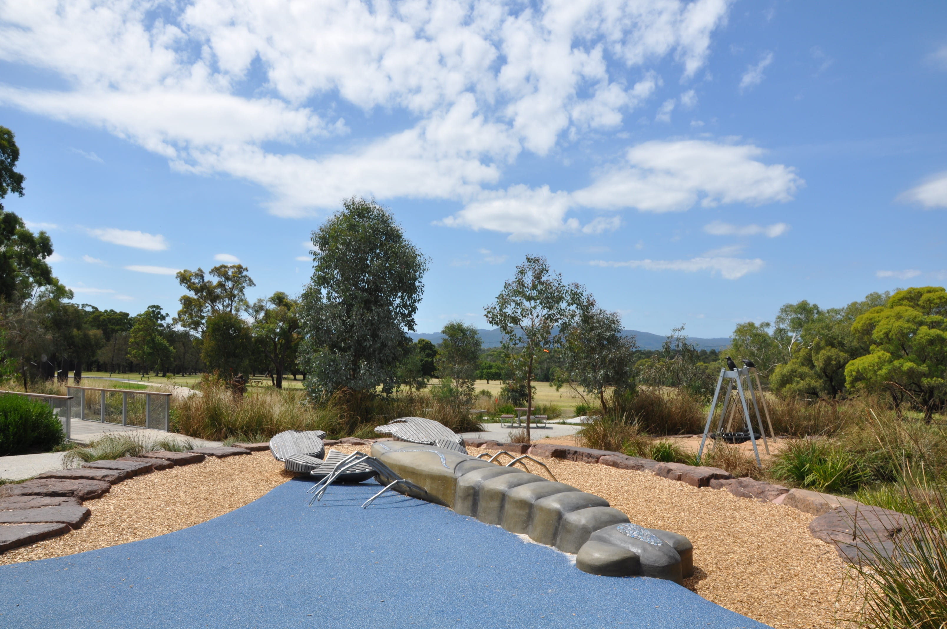 Playground with wide path and low metal play sculpture of a lizard