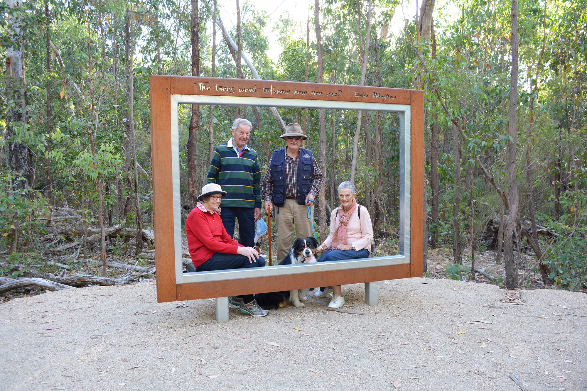 Four people and a dog standing inside a large metal photo frame in the bush