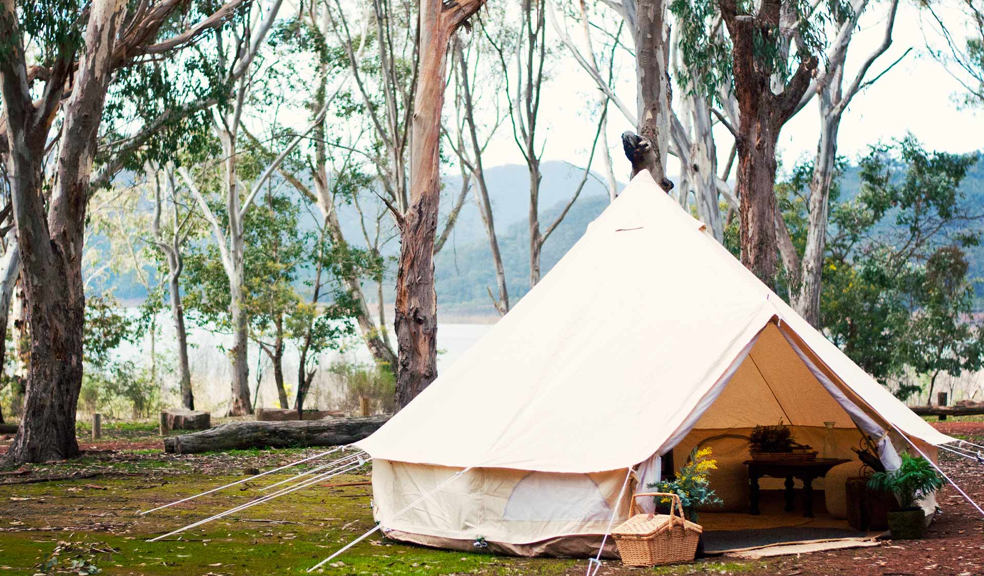 A canvas bell tent sits open with a lake visible in the background behind some trees