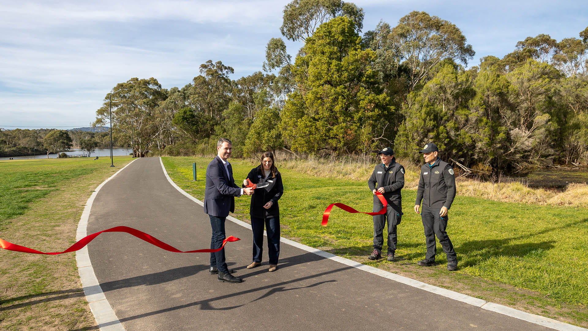 Two people cut a red ribbon opening a new paved trail 