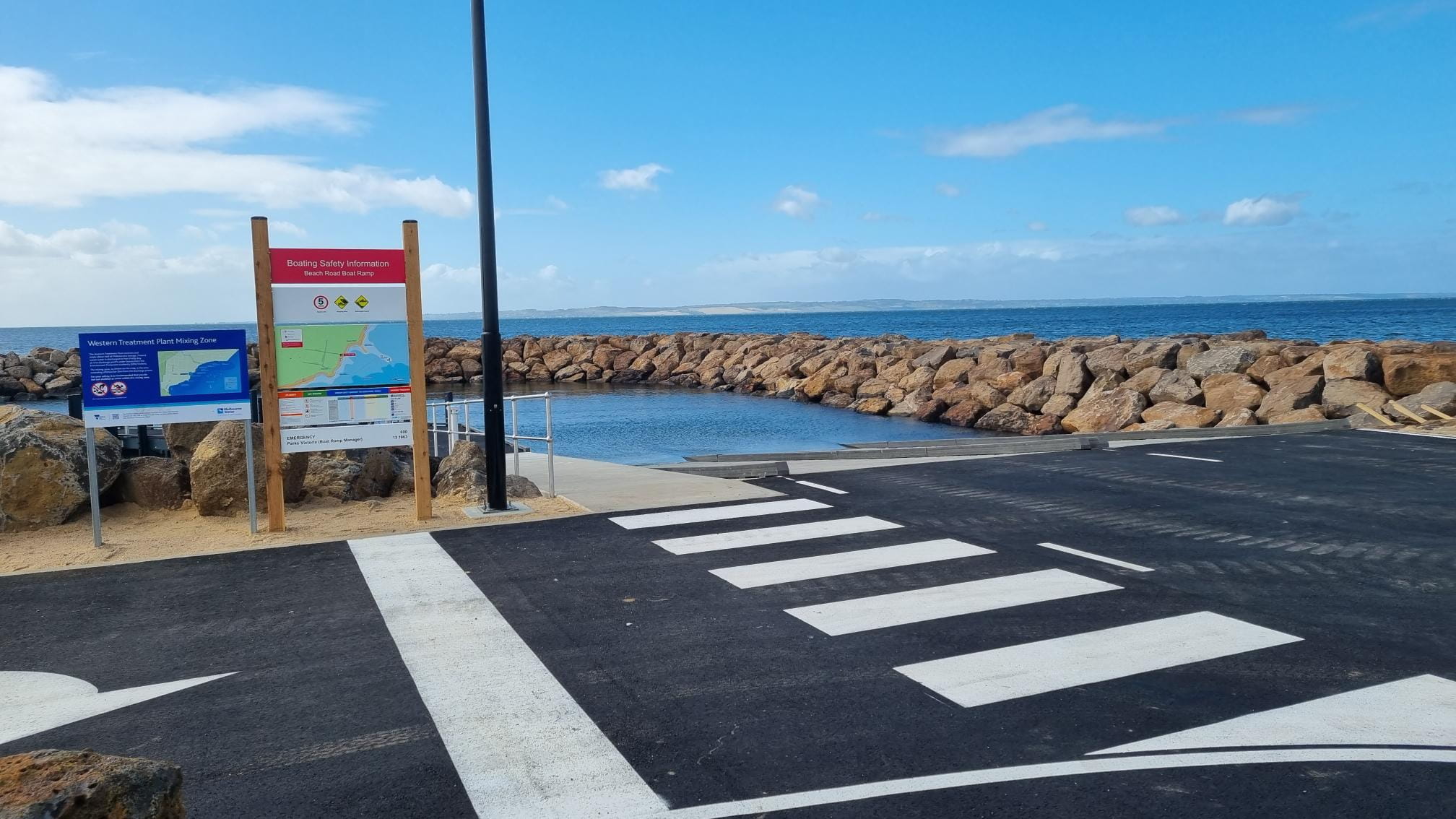 Boat ramp with signage and roadway in the foreground and breakwater in the background