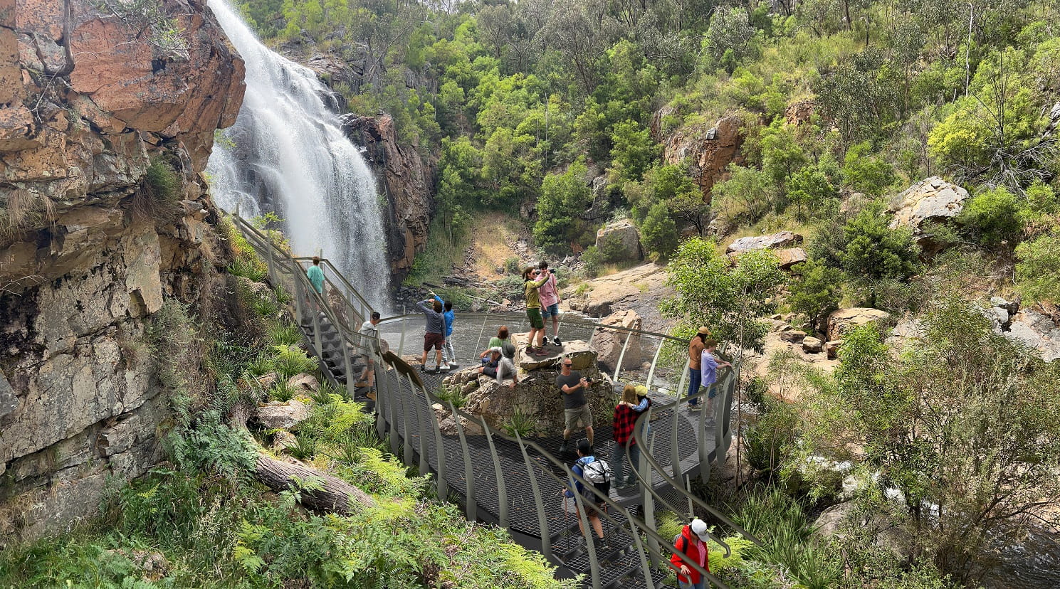 People standing on a viewing platform at the base of a waterfall in the background
