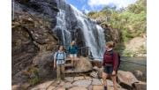 Three female walkers standing at viewing area on a track at the base of the waterfall, with the waterfall in the background