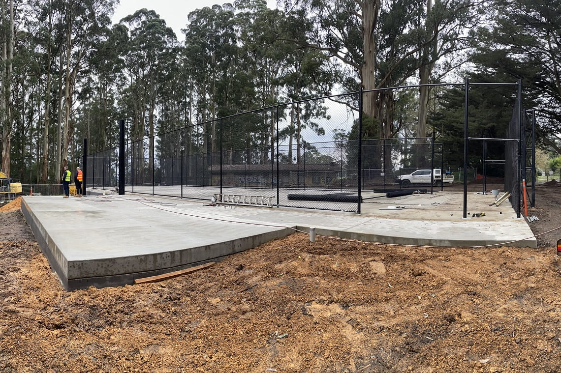 The construction of the cricket practice nets - a large concrete slabs sits on top of mud. Tall, black steel poles are erected around the boundary, where the net will be installed.