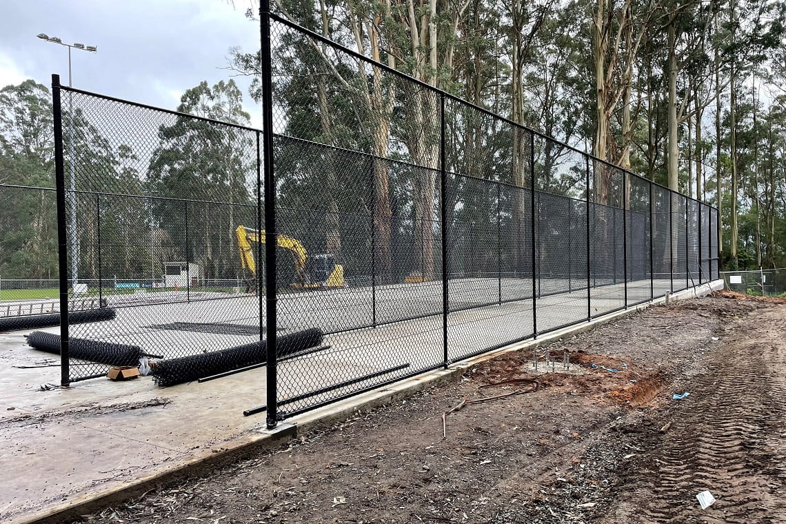 The construction of the cricket practice nets - a large concrete slabs sits on top of dirt. Tall, black steel poles are erected around the boundary, and net has been installed around the frame.
