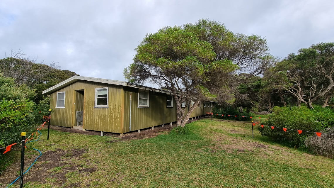 The site of the Point Nepean National Park campground expansion before demolition. An old yellow building sits among trees.