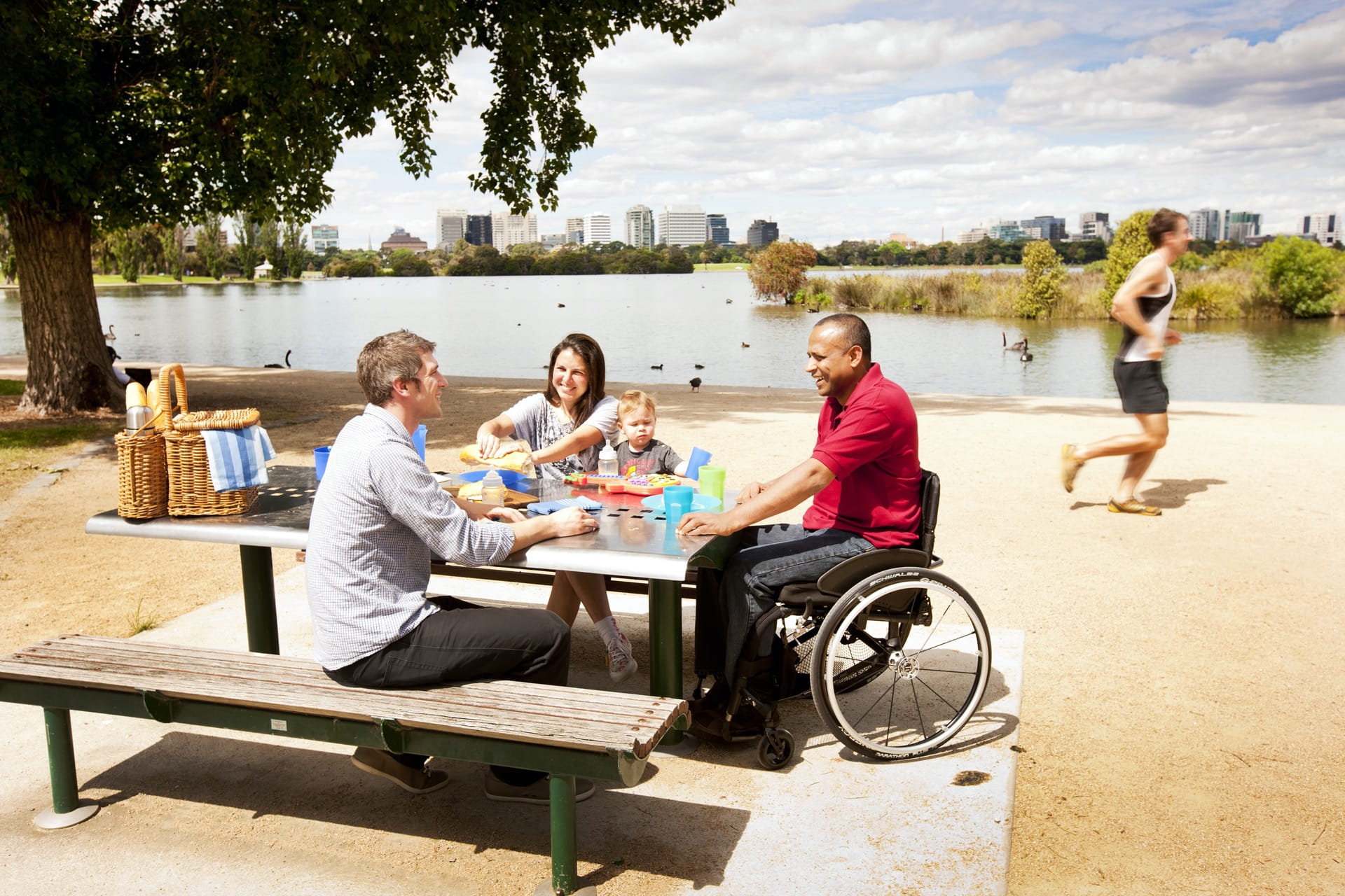 Three people eat lunch at a picnic table by a lake.