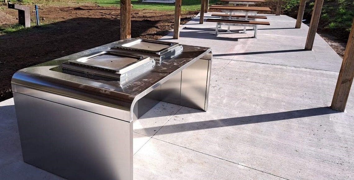 New all-abilities barbecue installed at Brimbank Park. The barbecue is underneath a shelter, on a big concrete slab. Picnic tables are in the background.