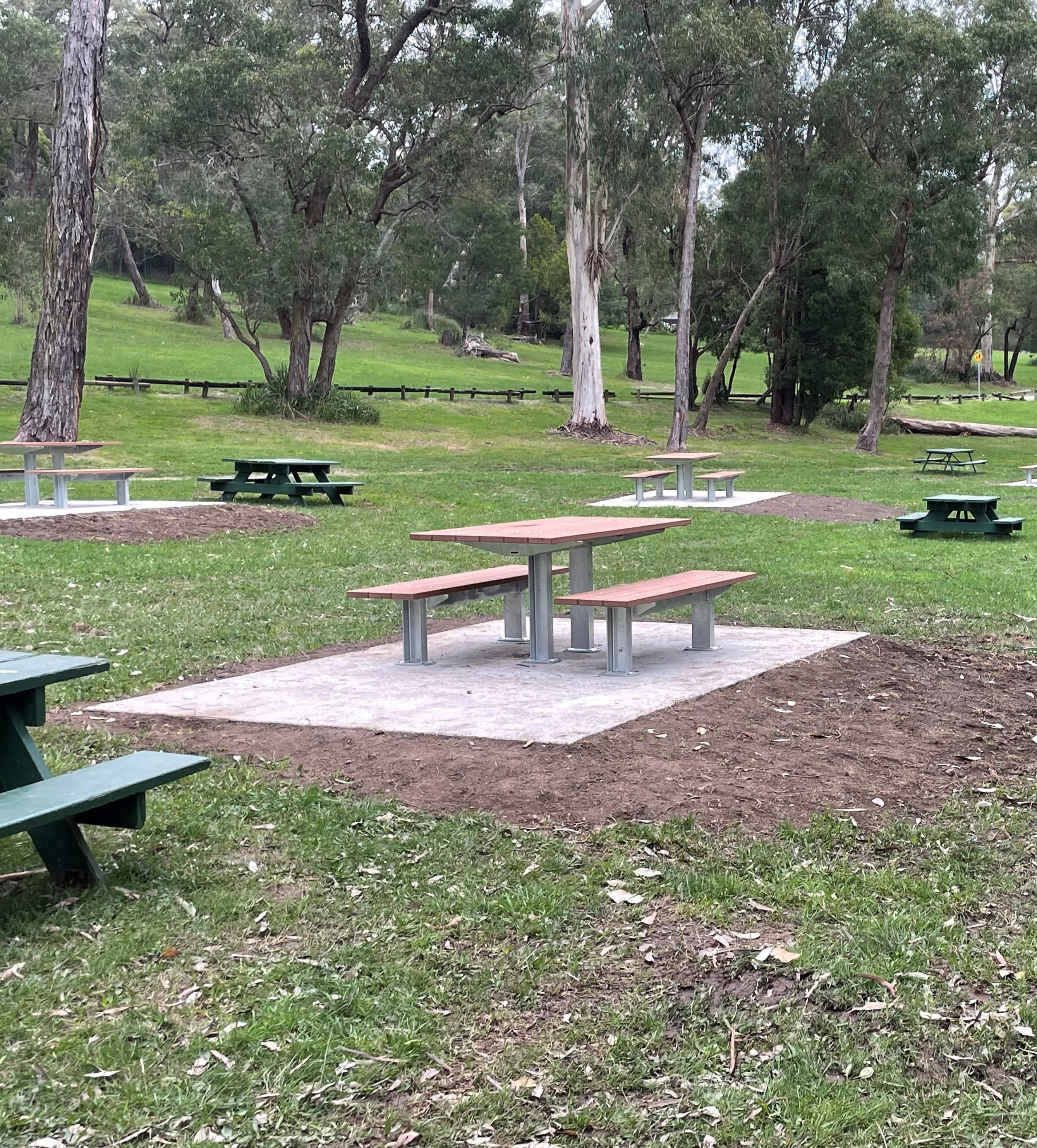 New picnic tables on concrete slabs among a grassed area in Maroondah Reservoir Park.