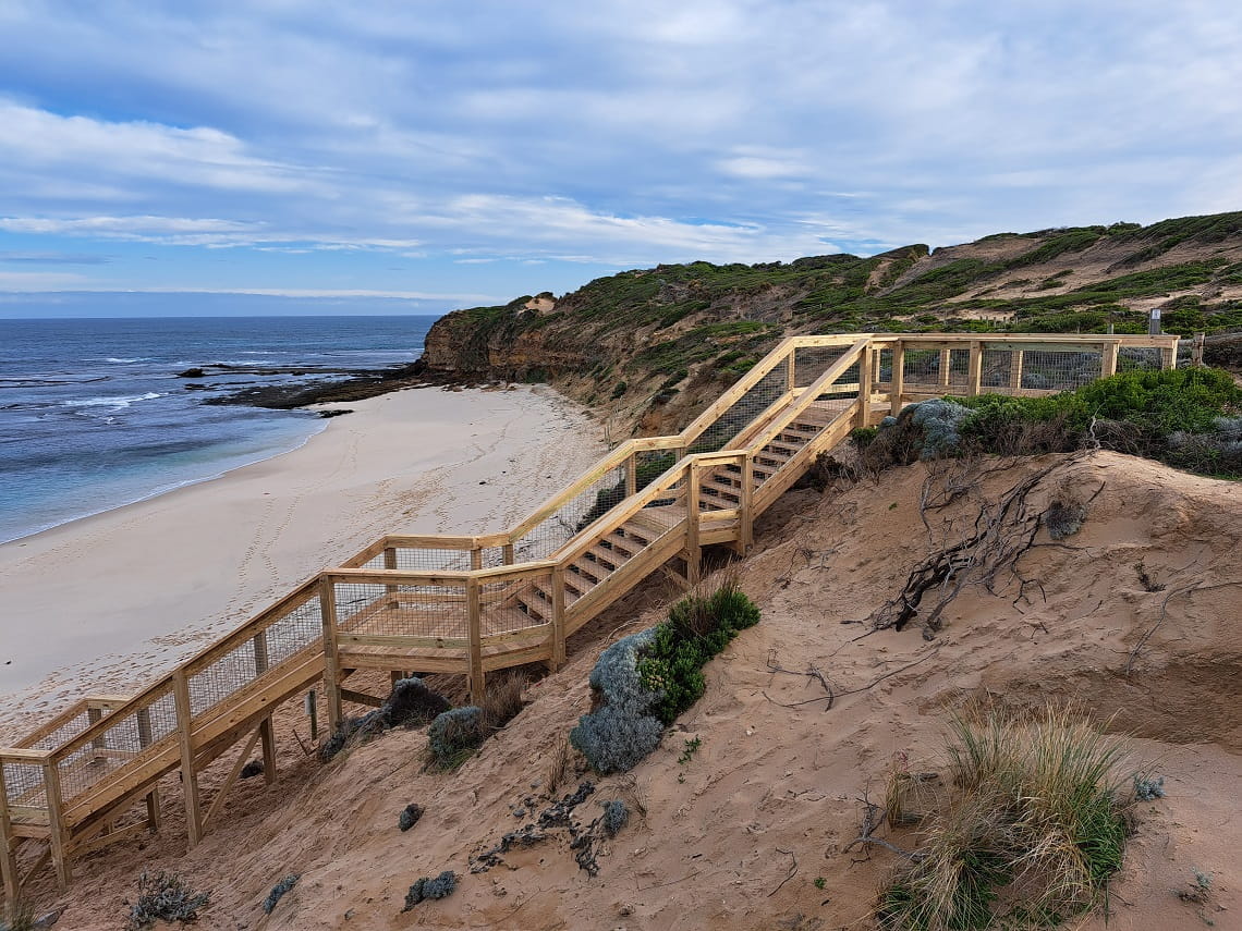 A side-on photo of the new stairs at Number 16 Beach. Wooden stairs lead from the top of grassy sand dunes, down to the beach.