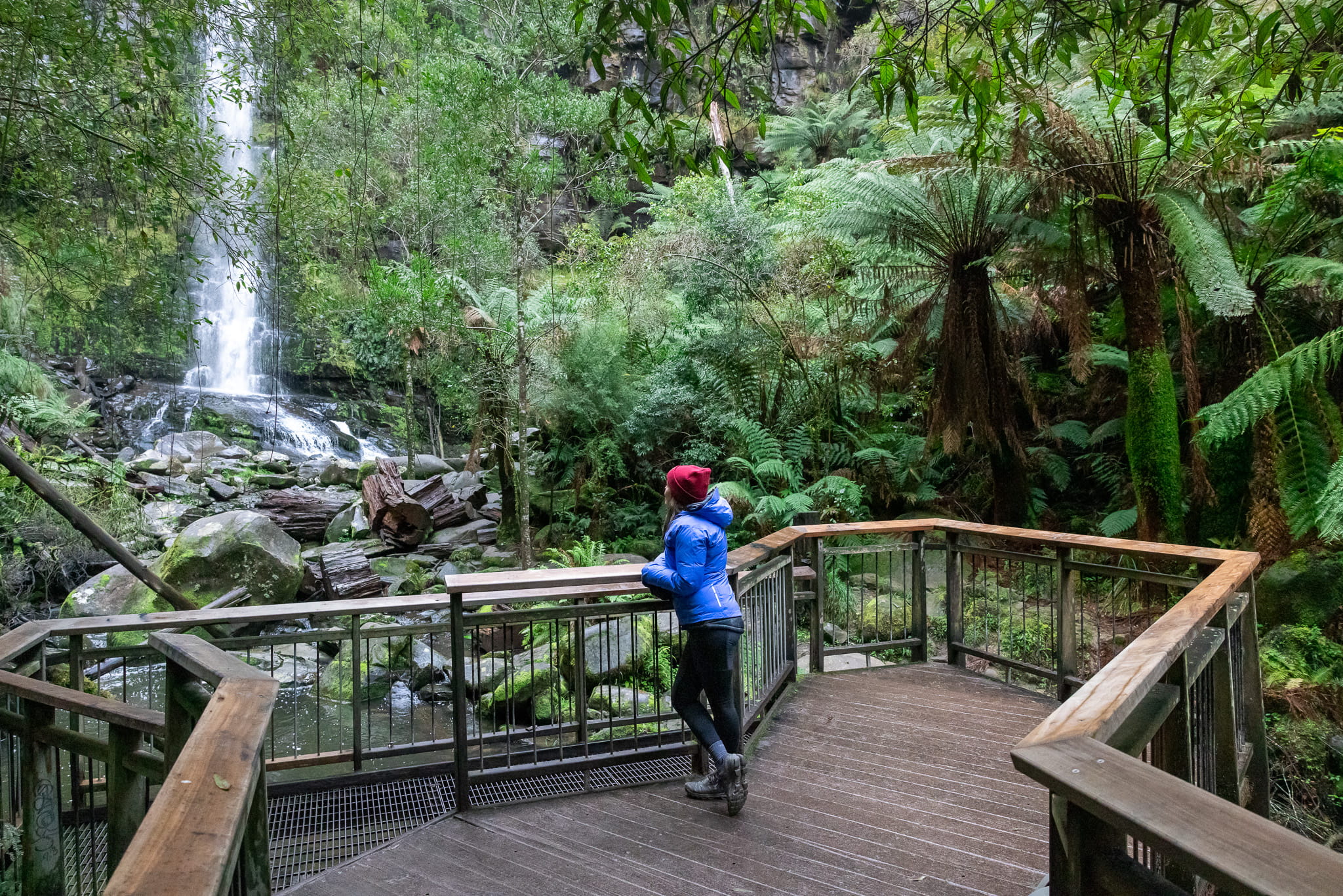 A woman looks at a waterfall from a viewing platform at the base of the waterfall