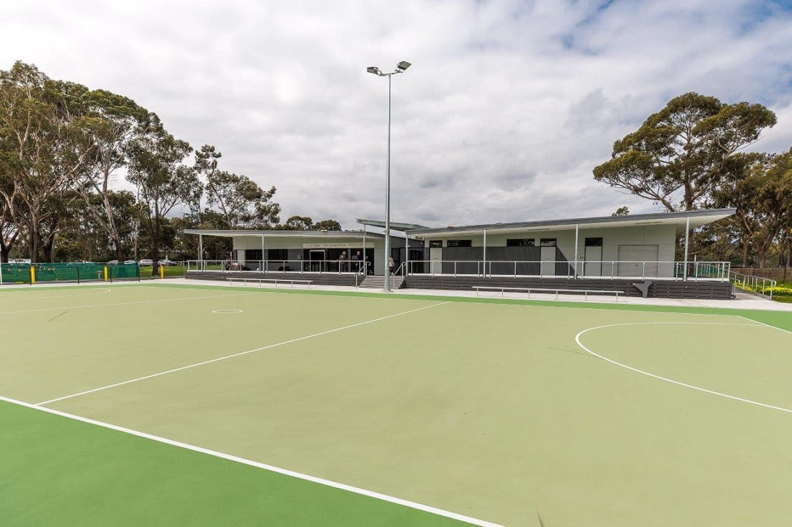 A large green netball court, with a grey pavilion in the background, located at Fairlea Reserve in Yarra Bend Park.