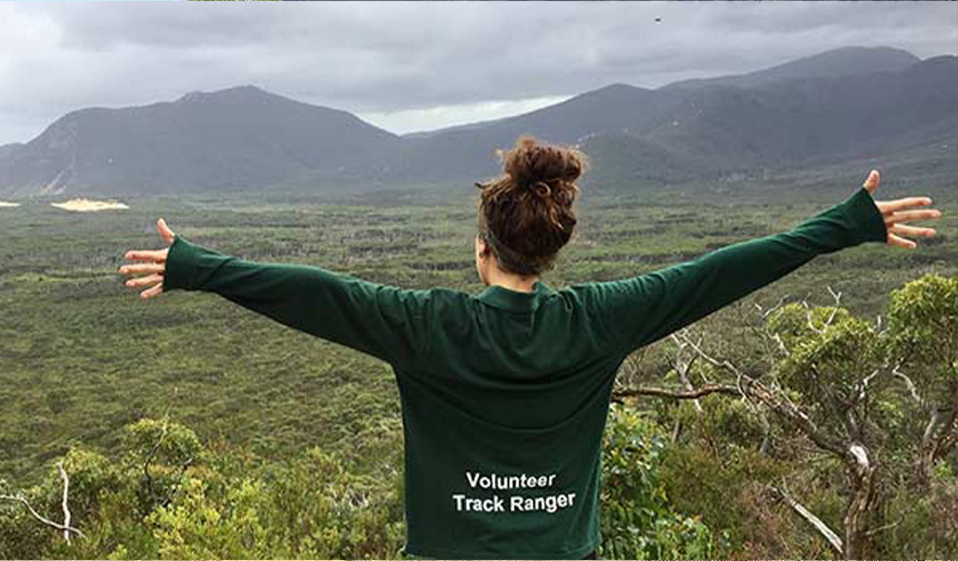 A women wearing a Volunteer Track Ranger top faces the view with her arms outstretched