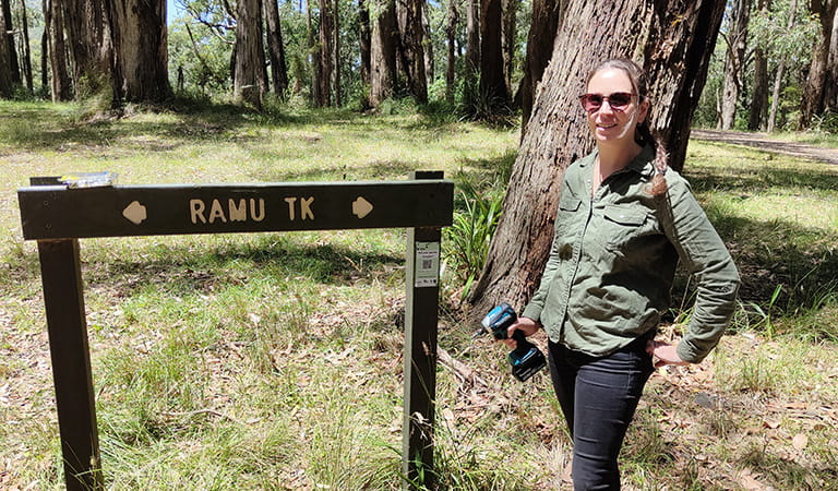 A woman in sunglasses stands next to a track sign holding a cordless drill.