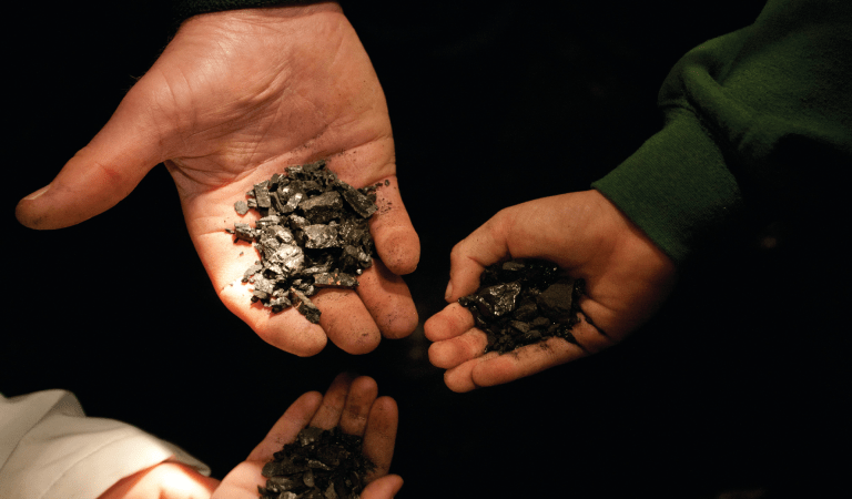Three hands holding small piles of coal