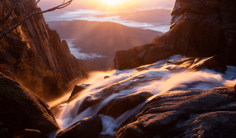 Waterfall running over rocks looking out to a sunrise