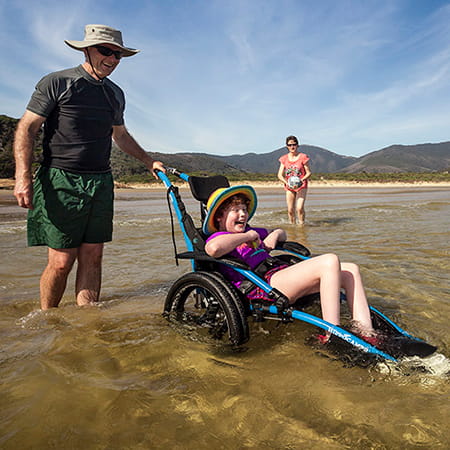 Man supporting someone in a beach wheelchair in shallow water