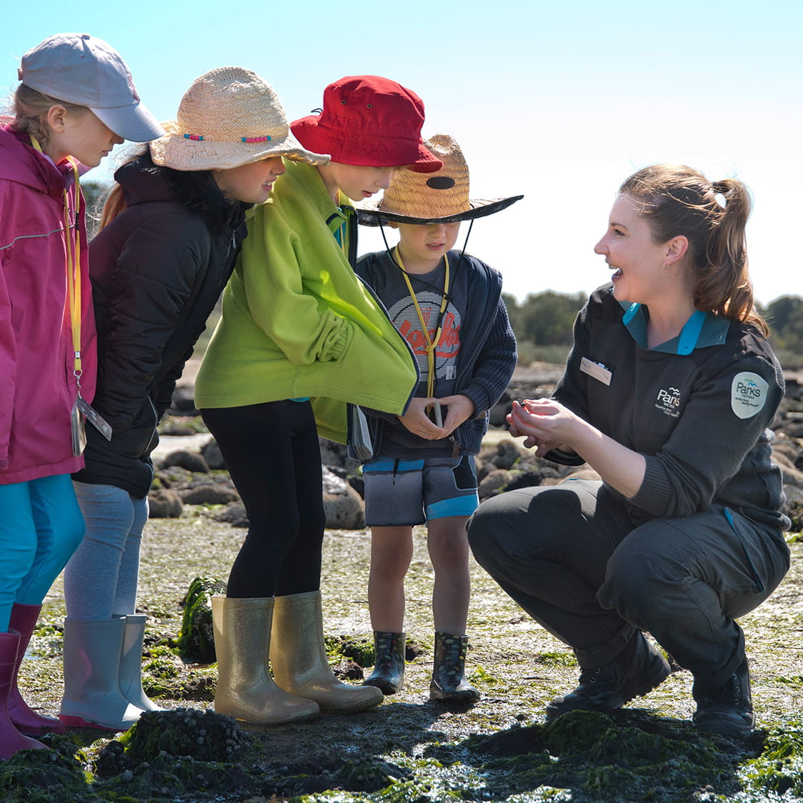 A group of kids wearing hats looking at something a laughing Ranger is holding in her hands.