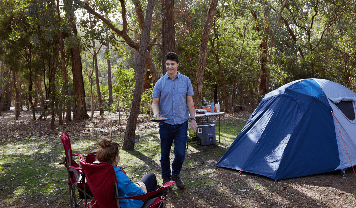 A man brings his girlfriend a plate of food while camping at Lakeside Campground, Lake Eildon National Park