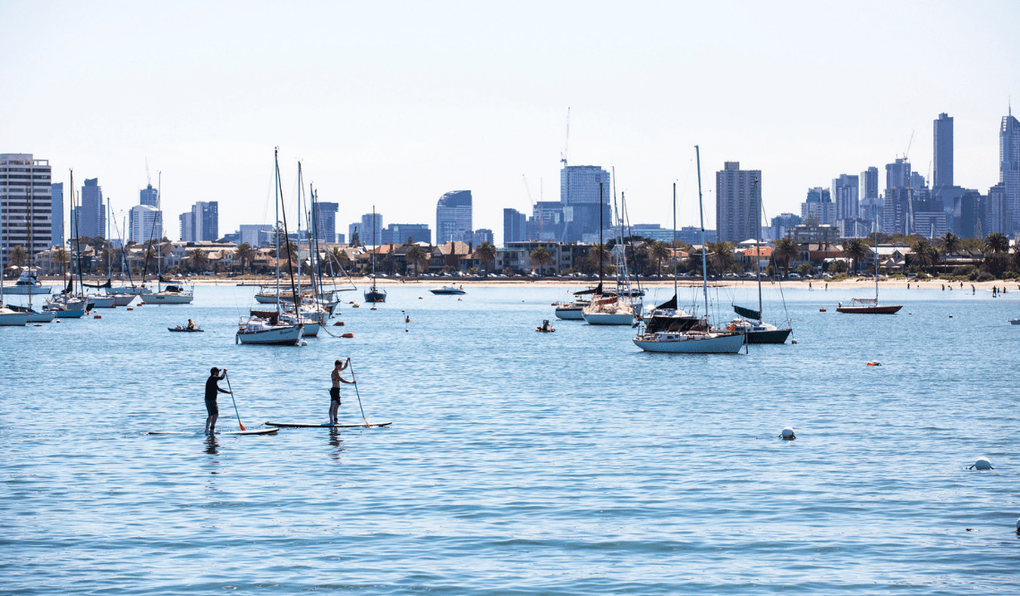 Two people standup paddleboarding on the bay with the city in the background