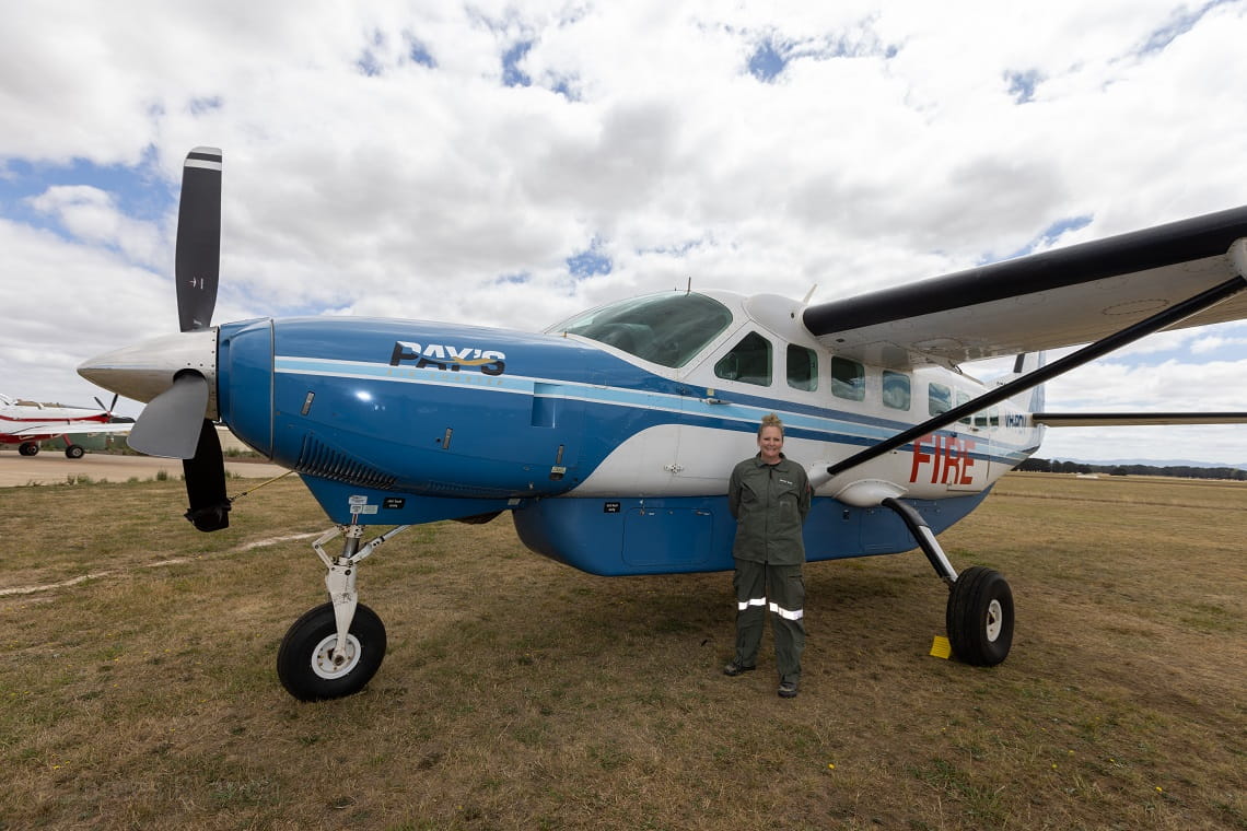 Rhianna stands under the wing of a small prop plane in her aviation uniform